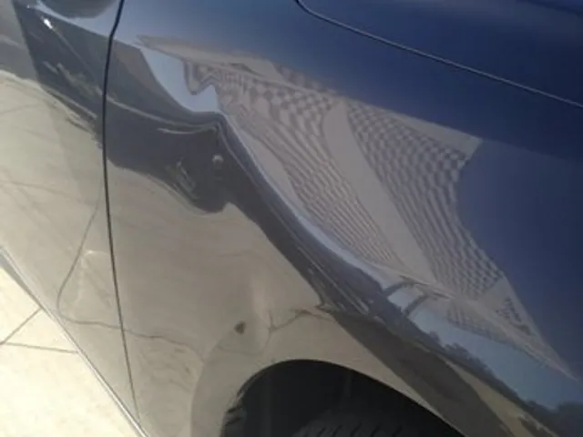 Dent shown in the reflection of a gray sedan quarter panel