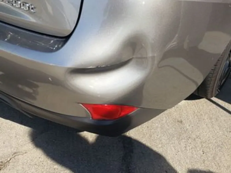 Champagne sedan rear bumper with a dent before repair